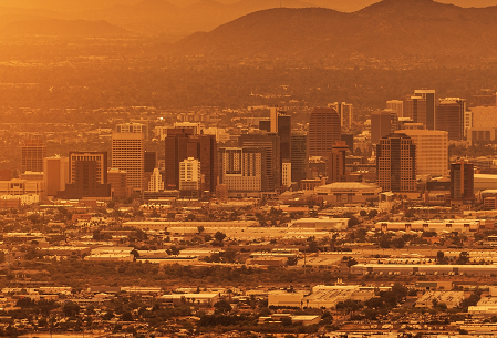 The Phoenix cityscape at sunset with skyscrapers and mountains in the background, all bathed in a warm, golden light.