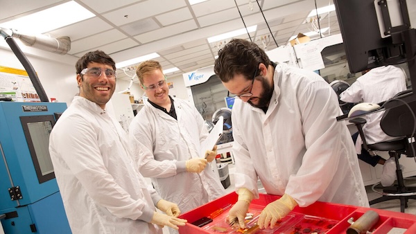 Nicholas Rolston, Hunter Mantle and Jacob Burrows in lab coats working and smiling in a laboratory.