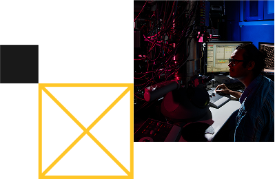 A man adjusts controls on an electron microscope with two computer screens in the background