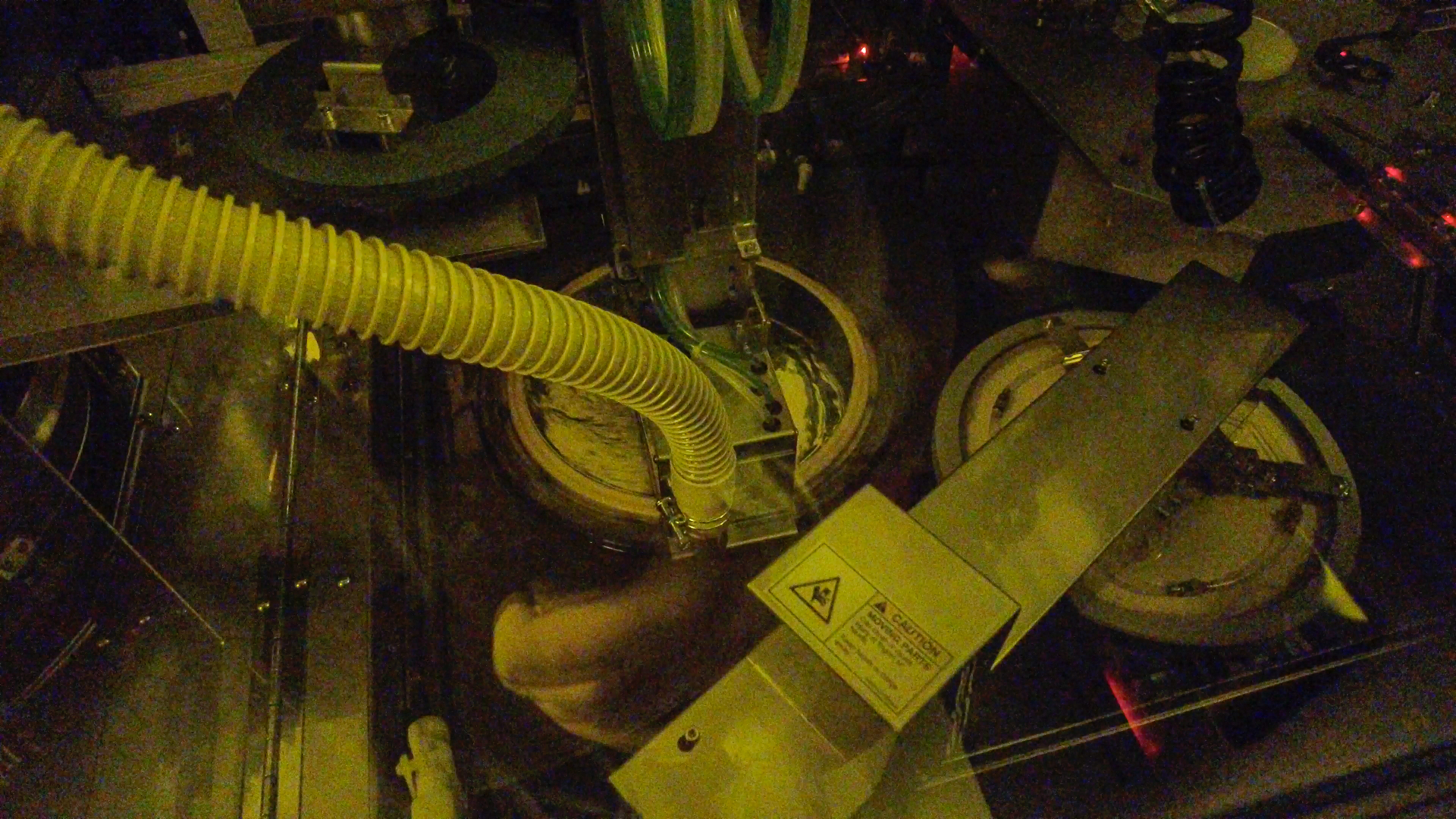 Inside view of a semiconductor wafer backgrinder and mounter with visible hoses, circular substrates, and machinery components in a softly lit environment.